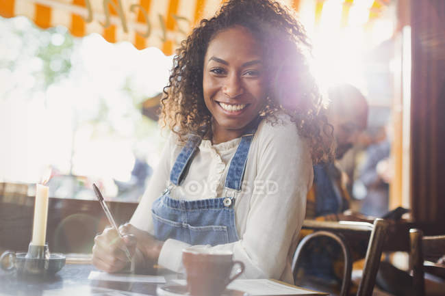 Ritratto sorridente giovane donna bere caffè e scrivere cartoline in caffè — Foto stock