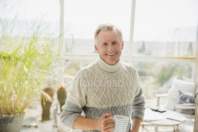 Portrait smiling senior man drinking coffee in beach house sunny sun porch — Stock Photo