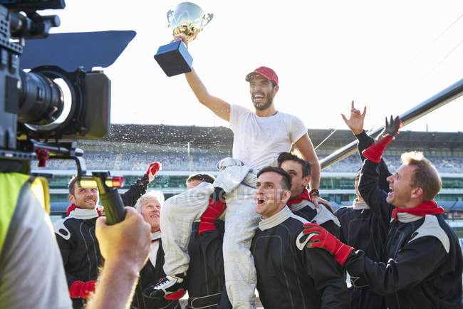 Racing team celebrating victory carrying race car driver with trophy on shoulders — Stock Photo