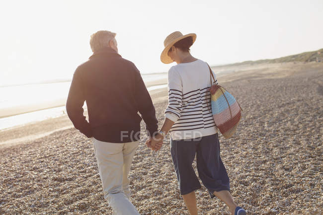 Ласковая зрелая пара, держащаяся за руки и идущая по солнечному пляжу — стоковое фото