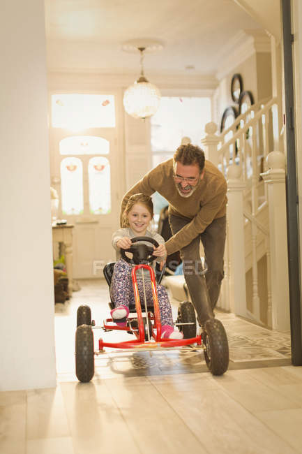Отец толкает дочь на игрушечной машине в коридоре фойе — стоковое фото