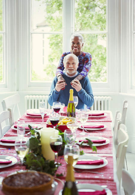 Retrato sonriendo multi-étnica pareja de ancianos en la mesa de la cena de Navidad - foto de stock