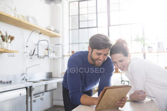 Jovem casal inclinado no balcão da cozinha e olhando para documentos — Fotografia de Stock