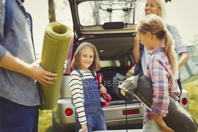 Retrato sorridente menina com a família descarregar equipamentos de acampamento de carro — Fotografia de Stock