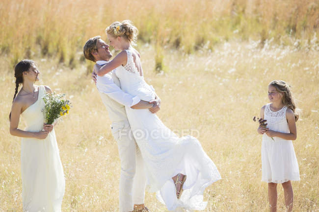Покоївка наречених і подруга наречених дивиться і сміється, молода пара обіймається на лузі — стокове фото