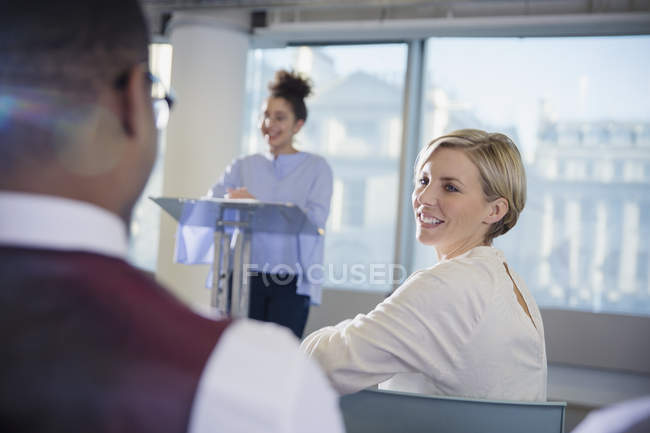 Mujer de negocios sonriente girando y escuchando a hombre de negocios en la audiencia de la conferencia - foto de stock