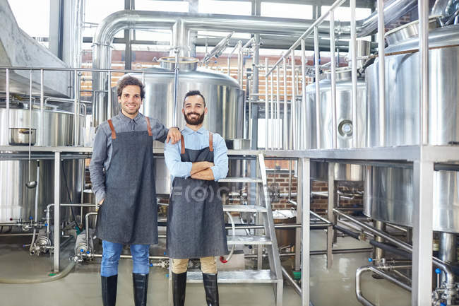 Портрет улыбающихся пивоваров в фартуках рядом с чанами — стоковое фото