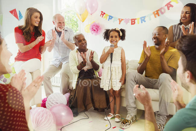 Багатоетнічна сім'я плескає для дівчини співає караоке з мікрофоном на вечірці на день народження — стокове фото