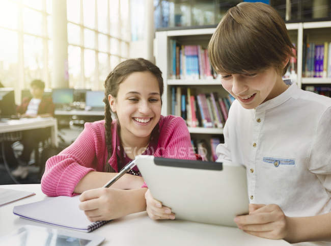 Усміхнені студенти вивчають, використовуючи цифровий планшет за столом у бібліотеці — стокове фото