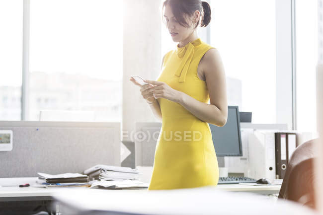 Empresária enviando mensagens com celular no escritório — Fotografia de Stock