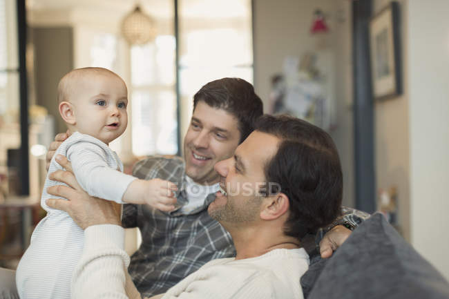 Male gay parents holding cute baby son on sofa — Stock Photo