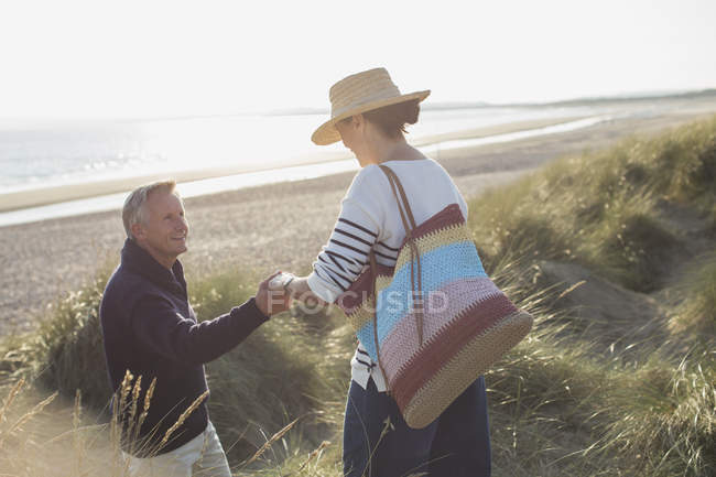 Esposo ayudando a la esposa en camino de hierba de playa soleado - foto de stock