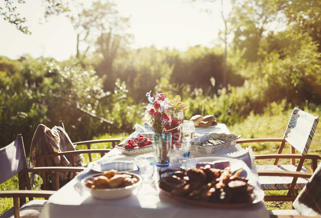 Comida e buquê de flores na mesa ensolarada jardim festa pátio — Fotografia de Stock