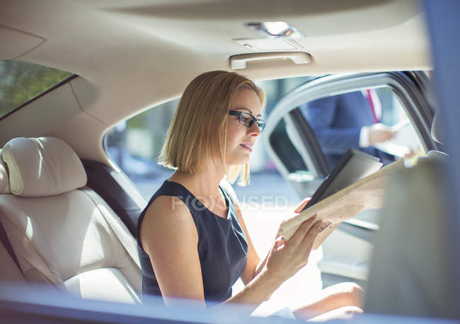 Femme d'affaires utilisant une tablette numérique sur le siège arrière de la voiture — Photo de stock