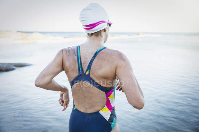 Mujer nadadora de aguas abiertas corriendo hacia el océano - foto de stock