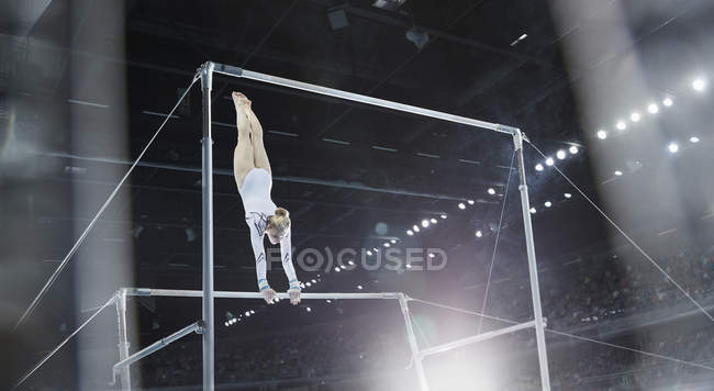 Female gymnast performing on uneven bars in arena — Stock Photo