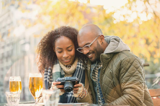 Young couple viewing digital camera and drinking beer at autumn sidewalk cafe — Stock Photo
