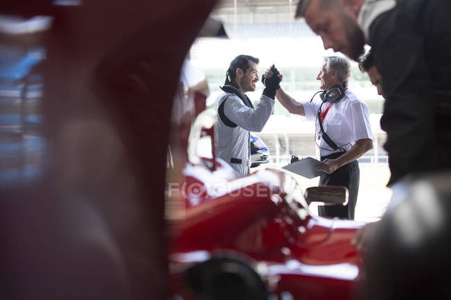 Gerente e fórmula um piloto de carro de corrida high-fiving na garagem de reparação — Fotografia de Stock