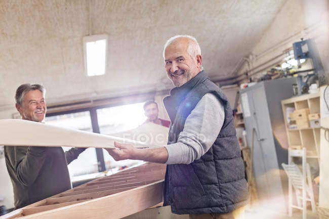 Portrait smiling senior male carpenter lifting wood boat in workshop — Stock Photo