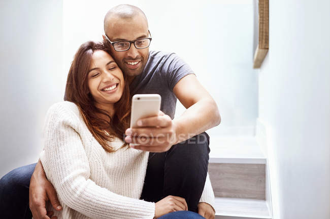 Улыбающаяся пара с камерой телефона делает селфи на лестнице — стоковое фото