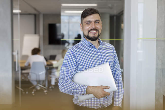 Portrait smiling businessman holding laptop in office — Stock Photo