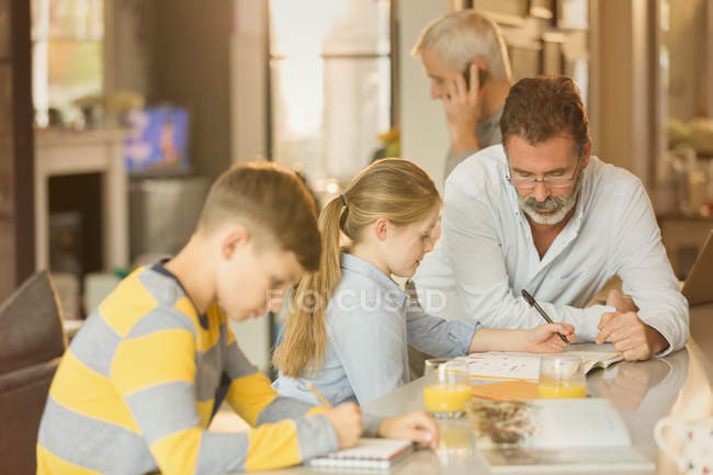 Male gay parents helping children with homework at counter — Stock Photo