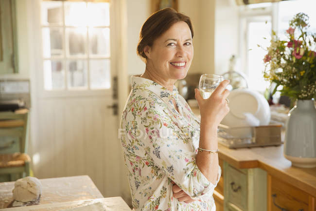 Портрет усміхненої зрілої жінки, що п'є вино на кухні — стокове фото