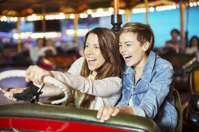 Дві веселі жінки на машині бампера їдуть в парку розваг — стокове фото