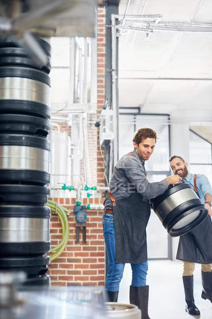 Male brewers carrying kegs in brewery — Stock Photo