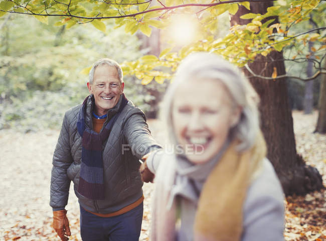 Игривая старшая пара, держащаяся за руки в осеннем парке — стоковое фото