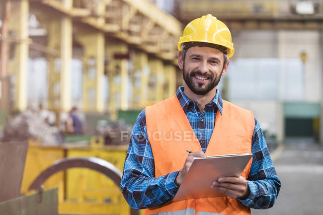 Porträt lächelnder Stahlarbeiter mit Klemmbrett in Fabrik — Stockfoto