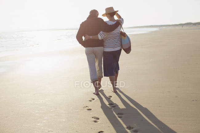 Зрелая пара обнимается и гуляет по солнечному пляжу — стоковое фото