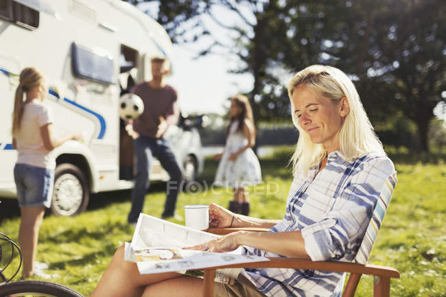 Lächelnde Frau liest Magazin und trinkt Kaffee vor sonnigem Wohnmobil — Stockfoto