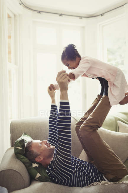 Батько багатоетнічного гра, балансування дочка на ніжках накладні витрати на дивані — стокове фото