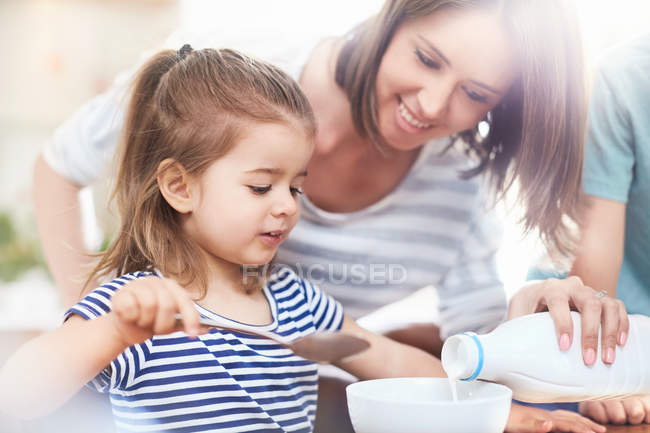 Tochter sieht zu, wie Mutter Milch in Müslischale gießt — Stockfoto