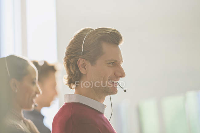 Smiling male telemarketer wearing headset talking on telephone — Stock Photo