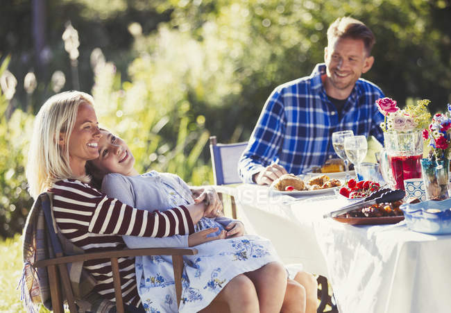 Sorrindo família afetuosa desfrutando de almoço no ensolarado jardim festa pátio mesa — Fotografia de Stock