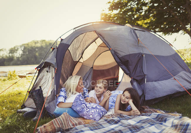 Madre e hijas hablando y relajándose en tienda de campaña en el camping - foto de stock