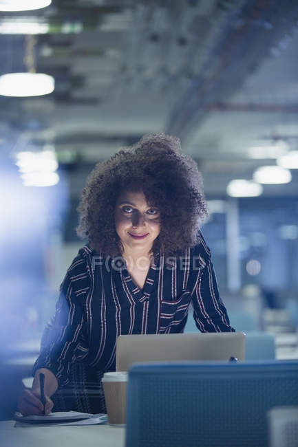 Портрет усміхненої впевненої бізнес-леді, що працює пізно в ноутбуці в темному офісі — стокове фото