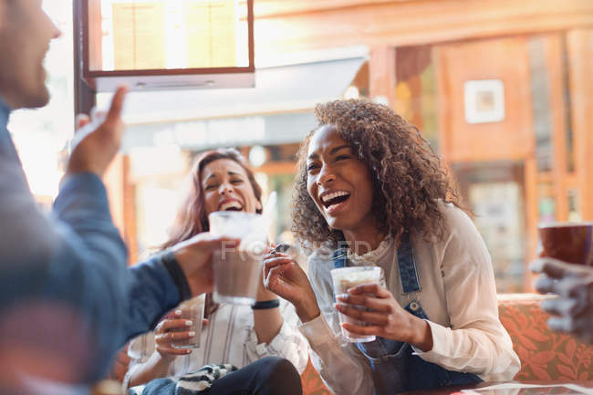 Laughing young friends drinking milkshakes in cafe — Stock Photo