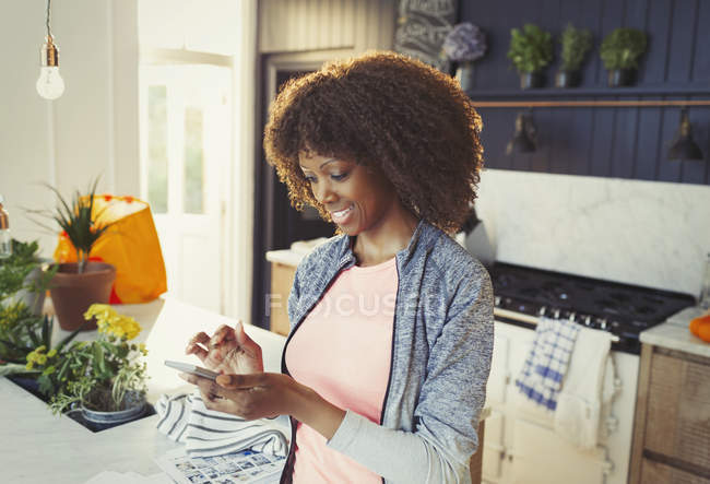 Женщина, использующая мобильный телефон на кухне — стоковое фото