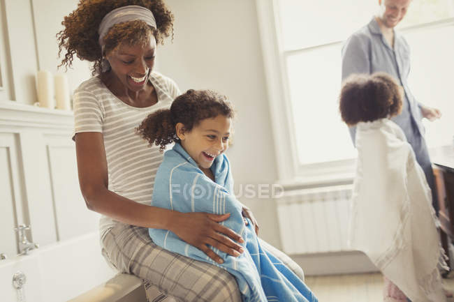 Беременная мать обертывание полотенце вокруг дочери после ванны в ванной комнате — стоковое фото