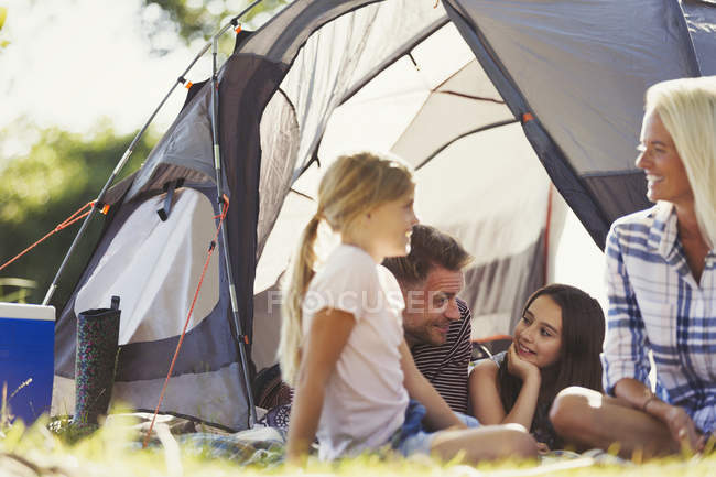 Famiglia sorridente che parla e si rilassa fuori tenda soleggiata — Foto stock