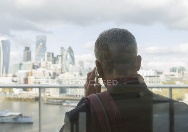 Empresario hablando por celular en balcón urbano con vista a la ciudad, Londres, Reino Unido - foto de stock