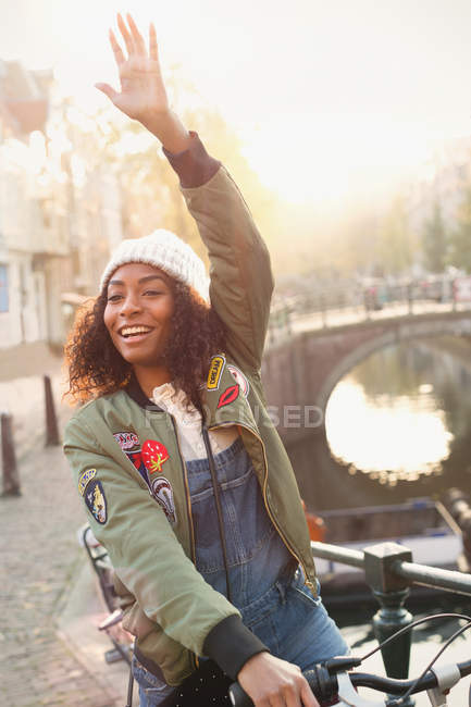Young woman on bicycle waving on urban street — Stock Photo
