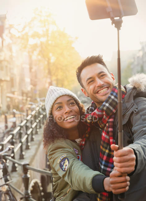Sorrindo jovem casal tomando selfie com vara selfie na rua urbana — Fotografia de Stock