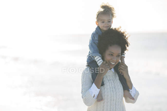 Mother carrying daughter on her shoulders on beach — Stock Photo