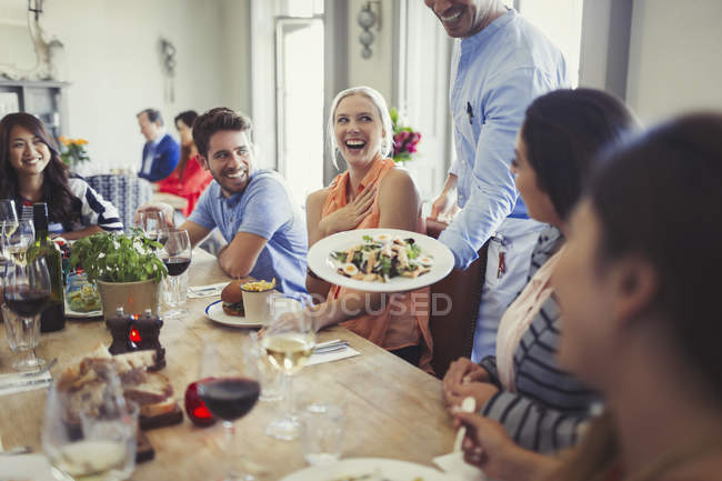 Waiter serving salad to woman dining with friends at restaurant table — Stock Photo