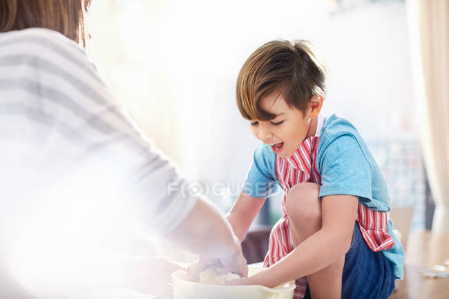 Усміхнений хлопчик допомагає мамі випікати, змішуючи тісто в мисці — стокове фото