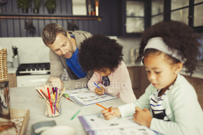 Multi-ethnic father and daughters coloring in kitchen — Stock Photo